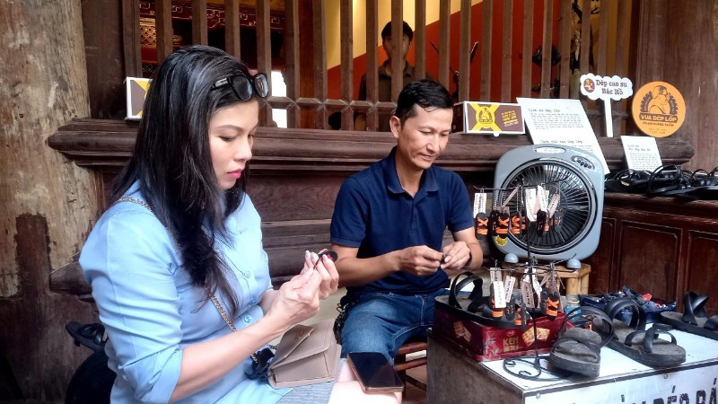 Khách tham quan tìm hiểu cách làm những chiếc dép cao-su mi-ni được dùng làm móc chìa khóa, quà tặng. Ảnh: Báo Nhân dân điện tử